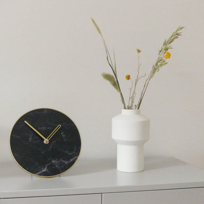 Een elegante wandklok met zwart marmeren wijzerplaat en goudkleurige wijzers. De minimalistische klok heeft een goudkleurige rand en het merk NEXtime, ideaal voor moderne interieurs en als decoratief element in woon- of kantoorruimtes.