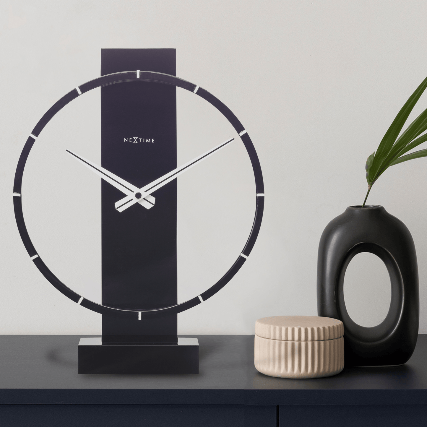 Een moderne, zwarte tafelklok van NexTime met een minimalistisch ontwerp, witte wijzers en een glanzende, cirkelvormige rand. Perfect voor een stijlvolle woonkamer of kantoordecoratie.