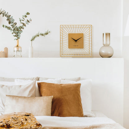Een goudkleurige wandklok met een minimalistisch ontwerp, een vierkante kast van metaal met zichtbare zonnestralen, en zwarte wijzers. Geschikt voor moderne interieurs en als decoratief element in woon- of kantoorruimtes.