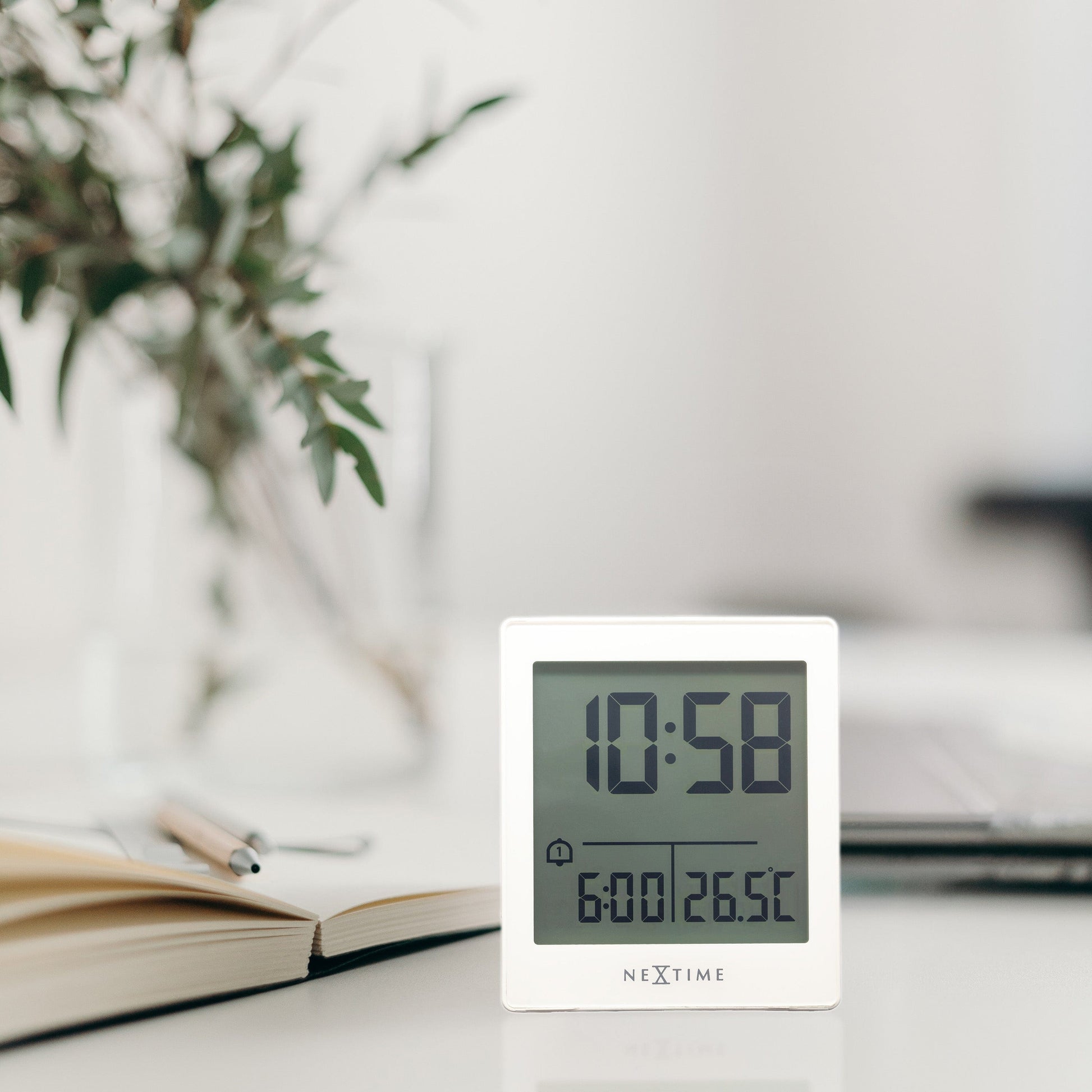 Een witte digitale wekker van NEXtime met een helder scherm dat 10:58 en 26.5°C toont, inclusief een alarminstelling. Geschikt voor kantoor- en huishoudelijke gebruik.