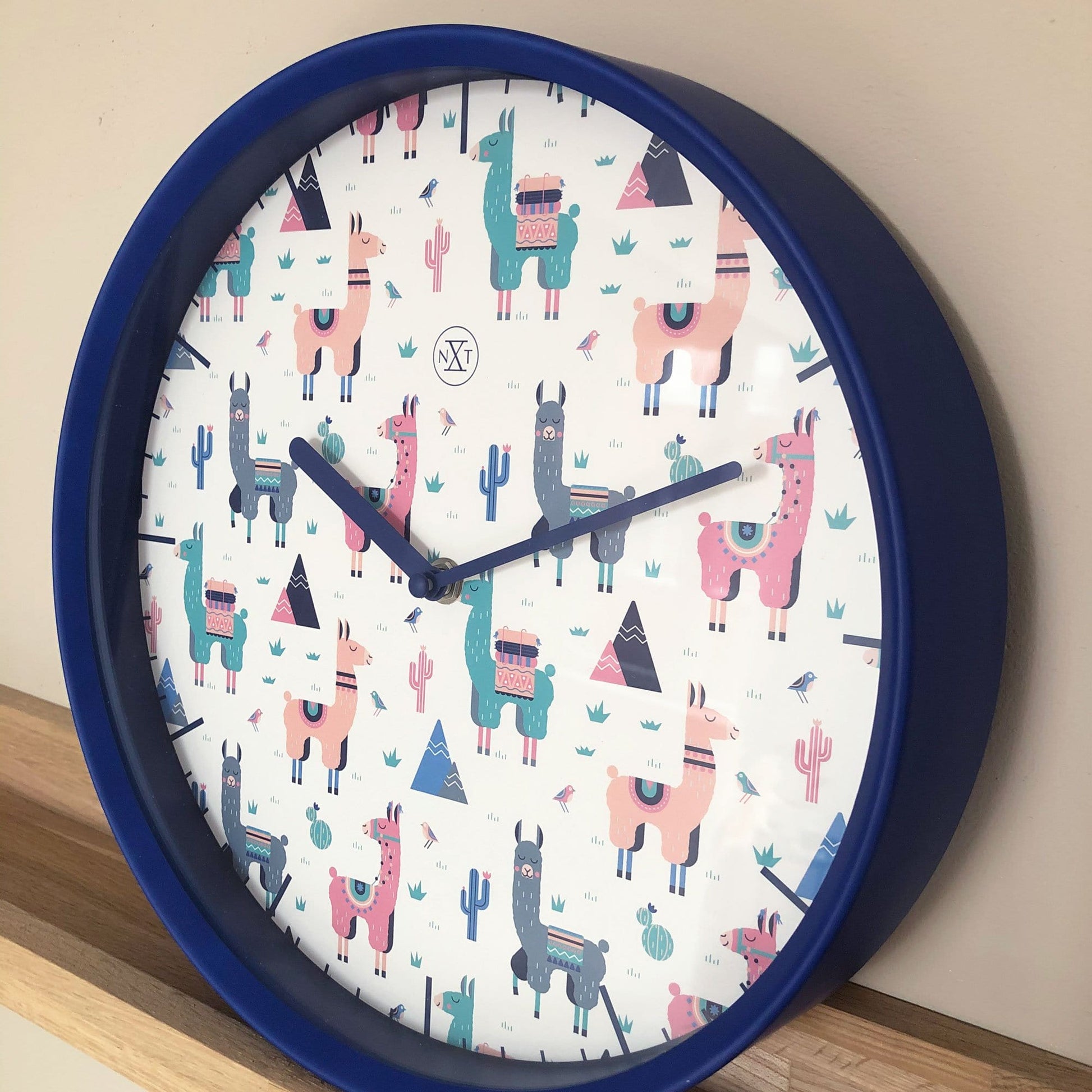 Een ronde wandklok met blauwe rand en kleurrijke alpaca-illustraties op witte achtergrond, perfect voor kinderkamer of speelruimte. Decoratieve klok met thema Andes en cactus, ideaal voor kinderinterieur.