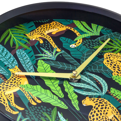 Een ronde wandklok met een zwart frame en een kleurrijk tropisch ontwerp van oranje leoparden tussen groene bladeren. Goudkleurige wijzers en een minimalistisch logo versterken de moderne, decoratieve stijl voor woonkamer of slaapkamer.
