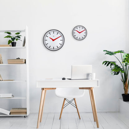 Een minimalistische wandklok met witte wijzerplaat, zwarte indexen en opvallende rode wijzers. Zilveren rand en het NXT-logo versterken de moderne, functionele stijl voor kantoor of woonruimte.