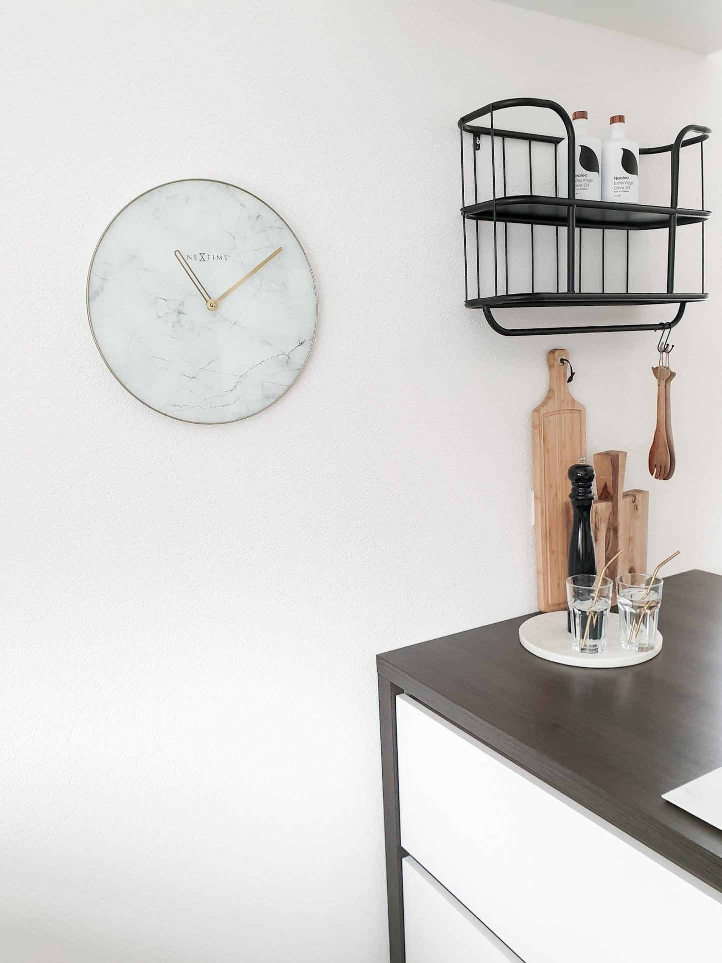 Een elegante wandklok met wit marmeren oppervlak en goudkleurige wijzers. De ronde klok heeft een goudkleurige rand en het merk 'NEXTIME' in het midden, ideaal voor moderne interieurs.