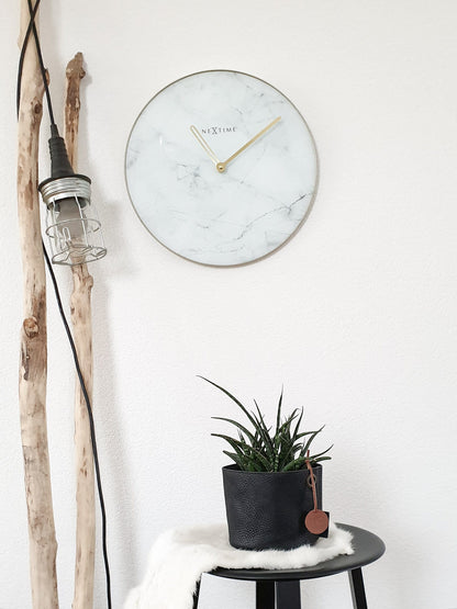 Een elegante wandklok met wit marmeren oppervlak en goudkleurige wijzers. De klok heeft een dunne gouden rand en het merk 'NEXTIME' in het midden, geschikt voor moderne interieurs.