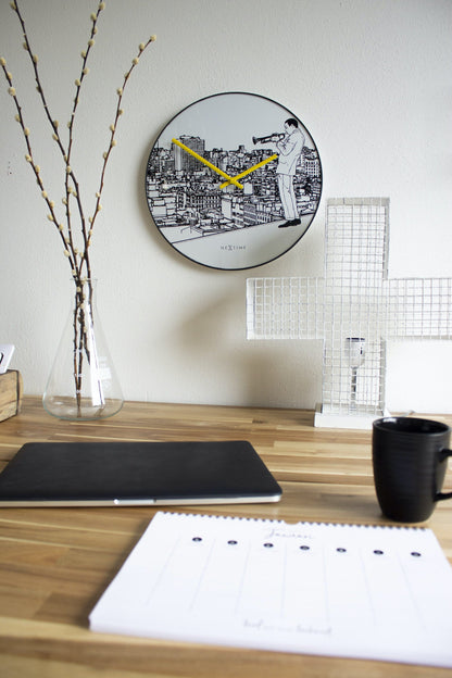 Een ronde wandklok met zwart-wit stadsillustratie en een muzikant met trompet. Geel wijzerplaat en zwarte kader, ideaal voor een moderne woonkamer of kantoordecoratie.