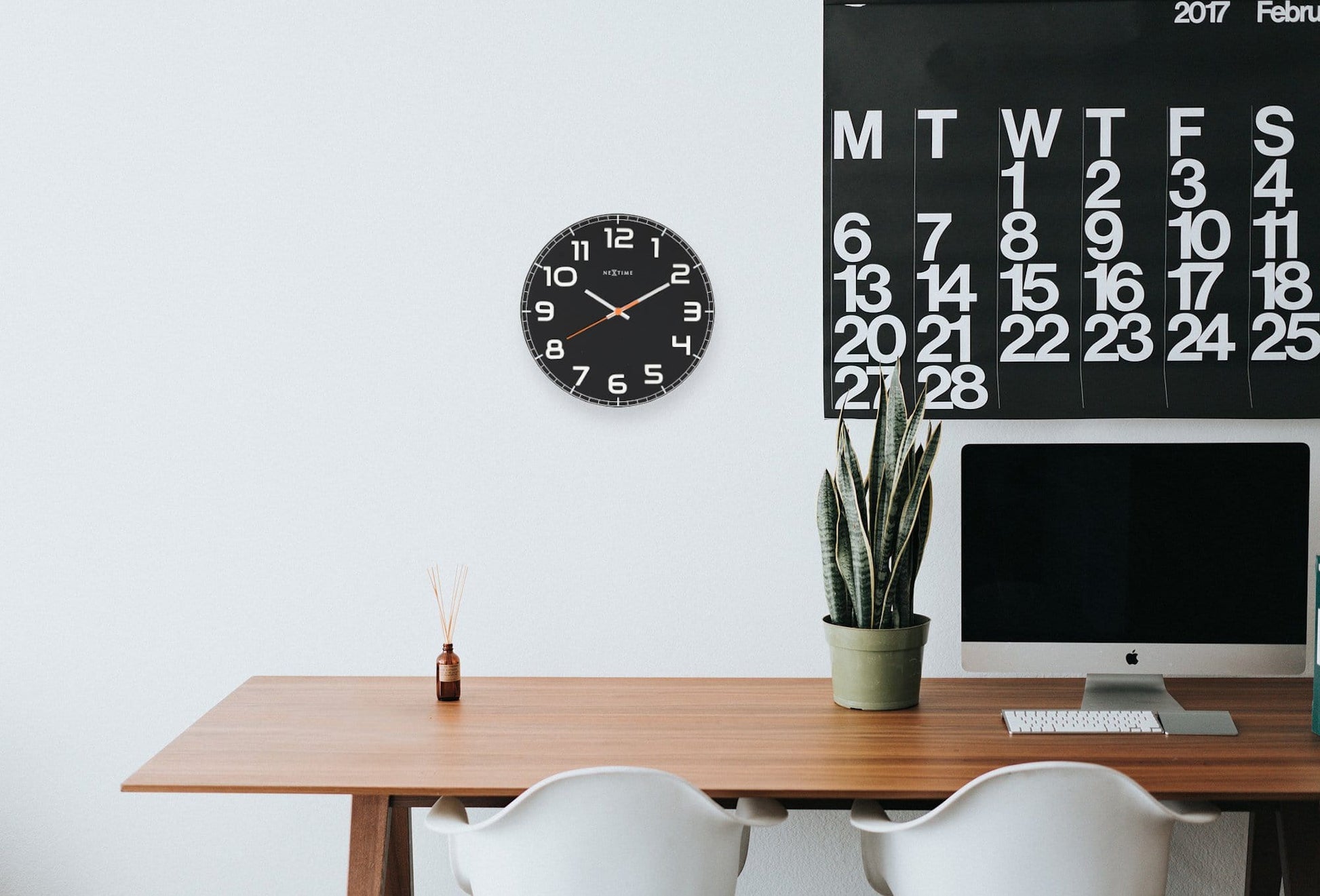 Een zwarte wandklok van Nextime met witte cijfers en een opvallende oranje secondewijzer, ideaal voor moderne interieurs. Geschikt voor woonkamer of kantoordecoratie met minimalistische stijl.