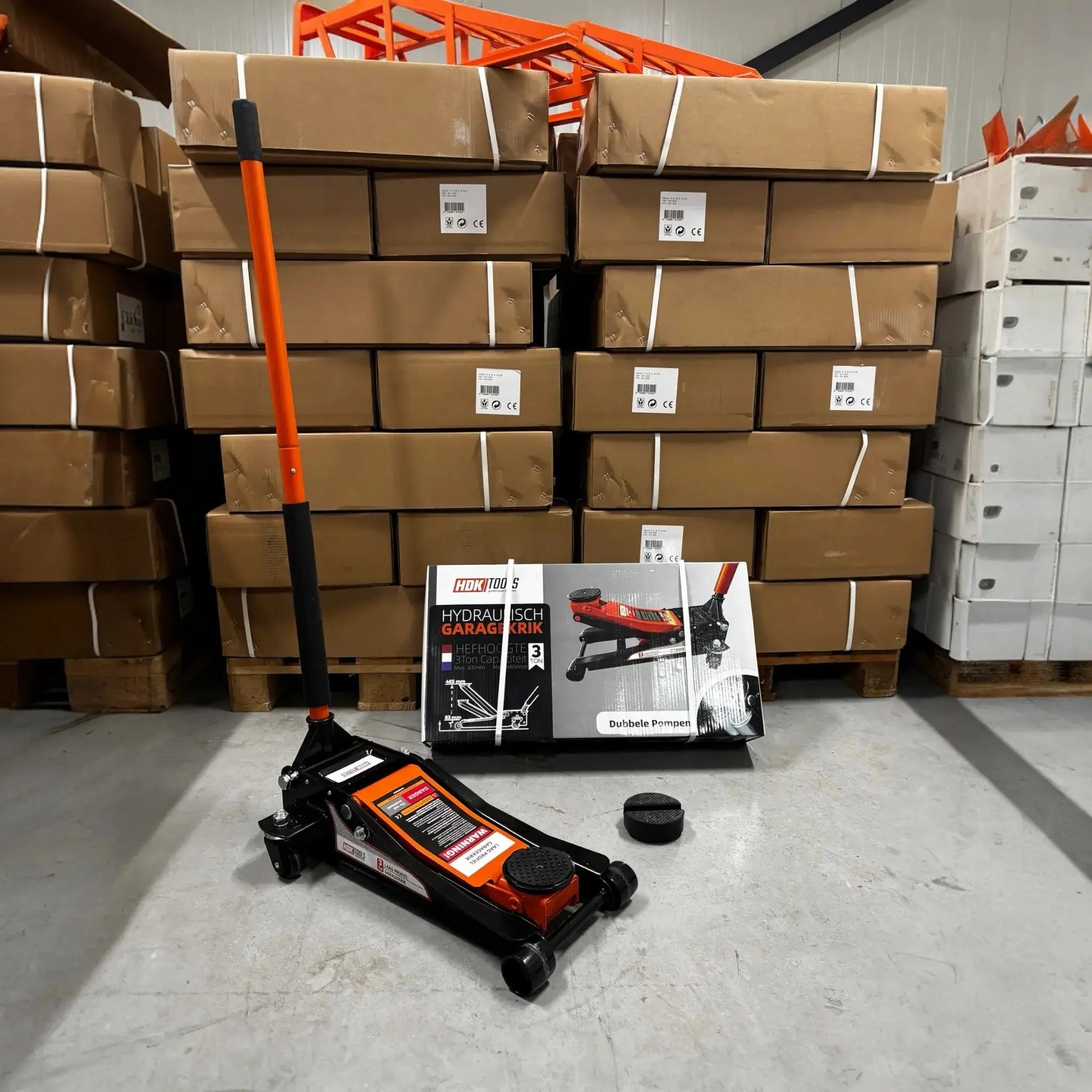 Oranje en zwarte hydraulische garagekrik met wieltjes, klaar voor gebruik in een professionele garage. Geschikt voor auto’s en andere zware voertuigen, met duidelijke merknaam op de verpakking.