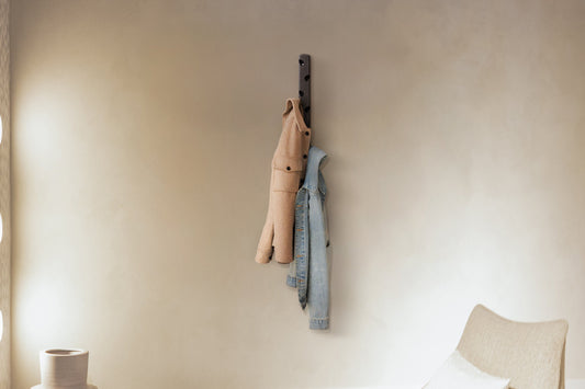 Een zwarte wandhanger met vier haken, waarop een beige wollen jas en een lichtblauwe denim jas hangen. Ideaal voor minimalistische interieurs en ruimtebesparende kledingopberging.