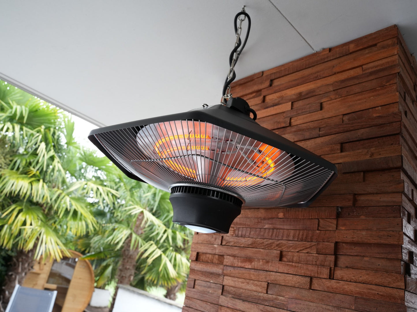 Zwarte hangende buitenverwarming met gloeiende infrarood-elementen en een ketting, geschikt voor terrassen en tuinen. Model van het merk AVOID, met bedieningsknop en veiligheidsafdekking.