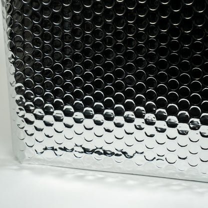 Zilverkleurige, opgevouwen isolatiemantel met hexagonaal patroon, naast een rol lichtgeel isolatieband. Geschikt voor thermische isolatie in bouw- en renovatieprojecten.