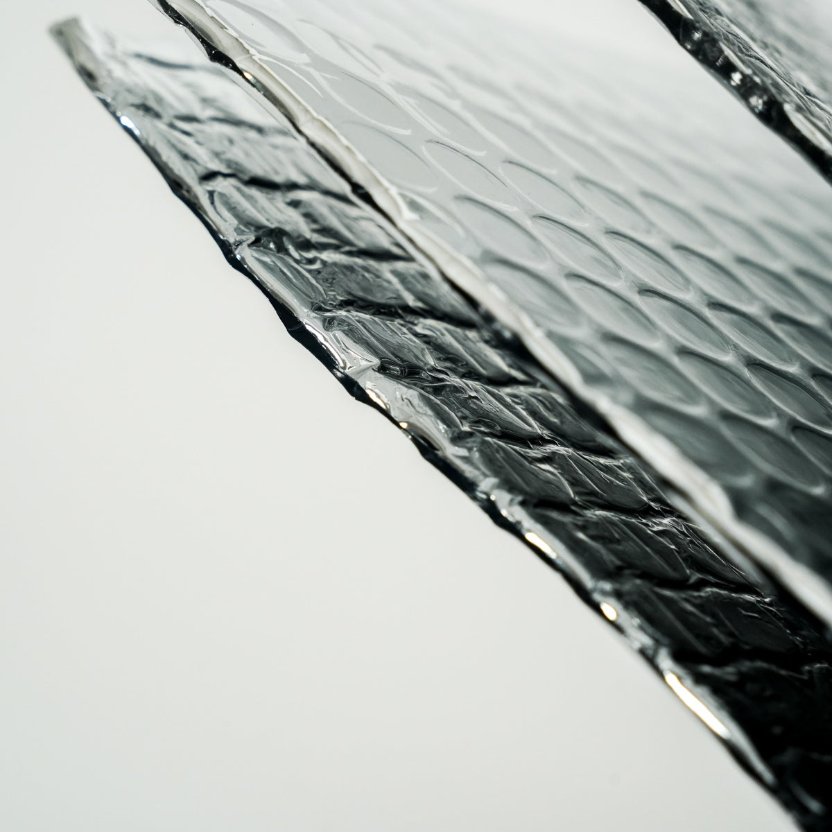 Zilverkleurige, opgevouwen isolatiemateriaal met hexagonale textuur, klaar voor gebruik. Achtergrond toont het materiaal in platte vorm, vergezeld van een rol beige tape voor montage.