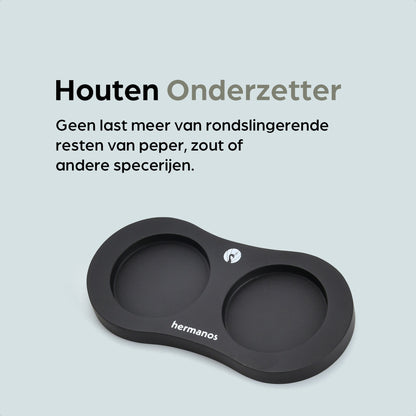 Zwarte houten pepermolen en zoutmolen met goudkleurige doppen, geplaatst op een zwarte standaard met het merk 'hermanos'. Inclusief vier vervangende doppen voor keukengebruik.