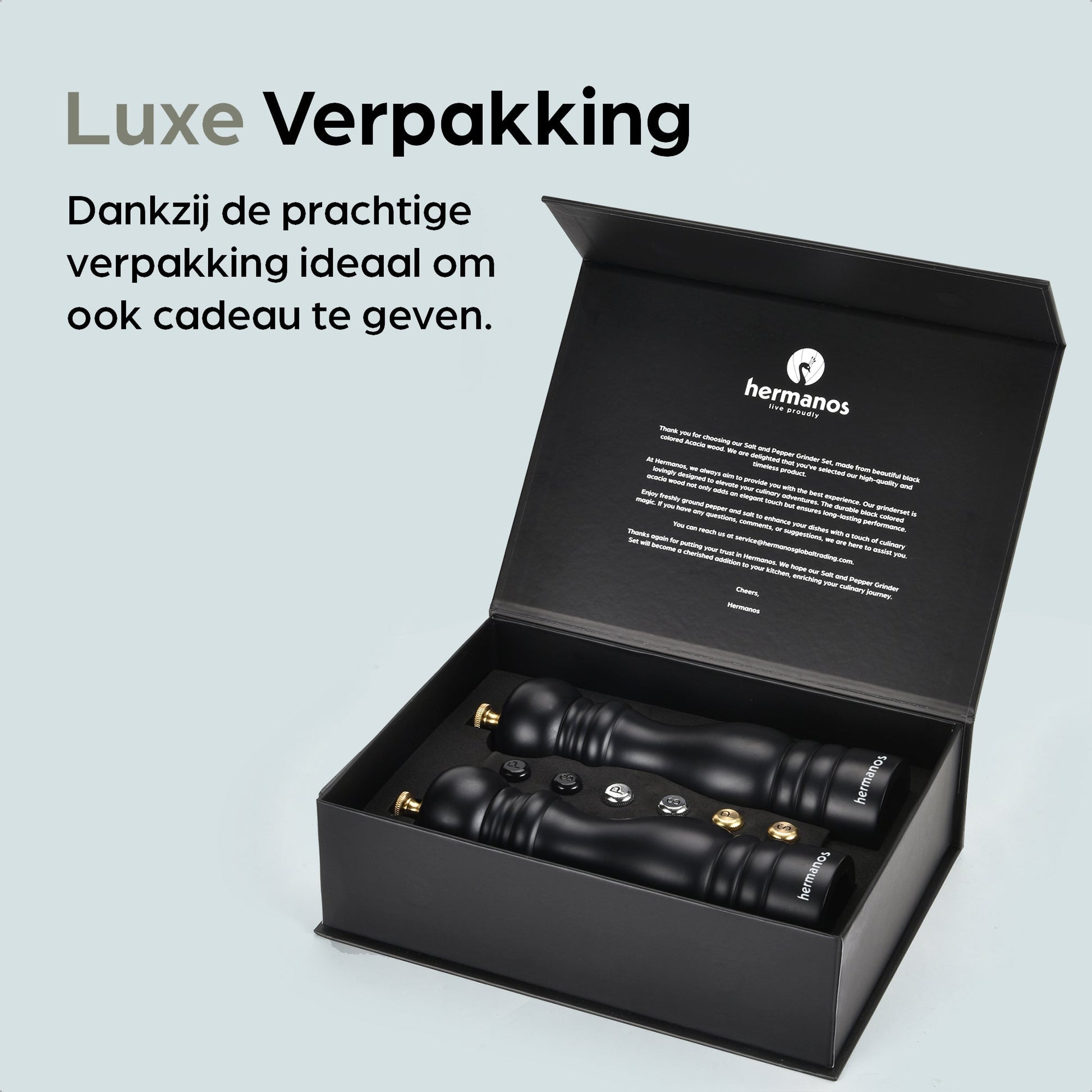Zwarte houten pepermolen en zoutmolen met goudkleurige doppen, geplaatst op een zwarte standaard met het merk 'hermanos'. Inclusief vier vervangende doppen voor keukengebruik.