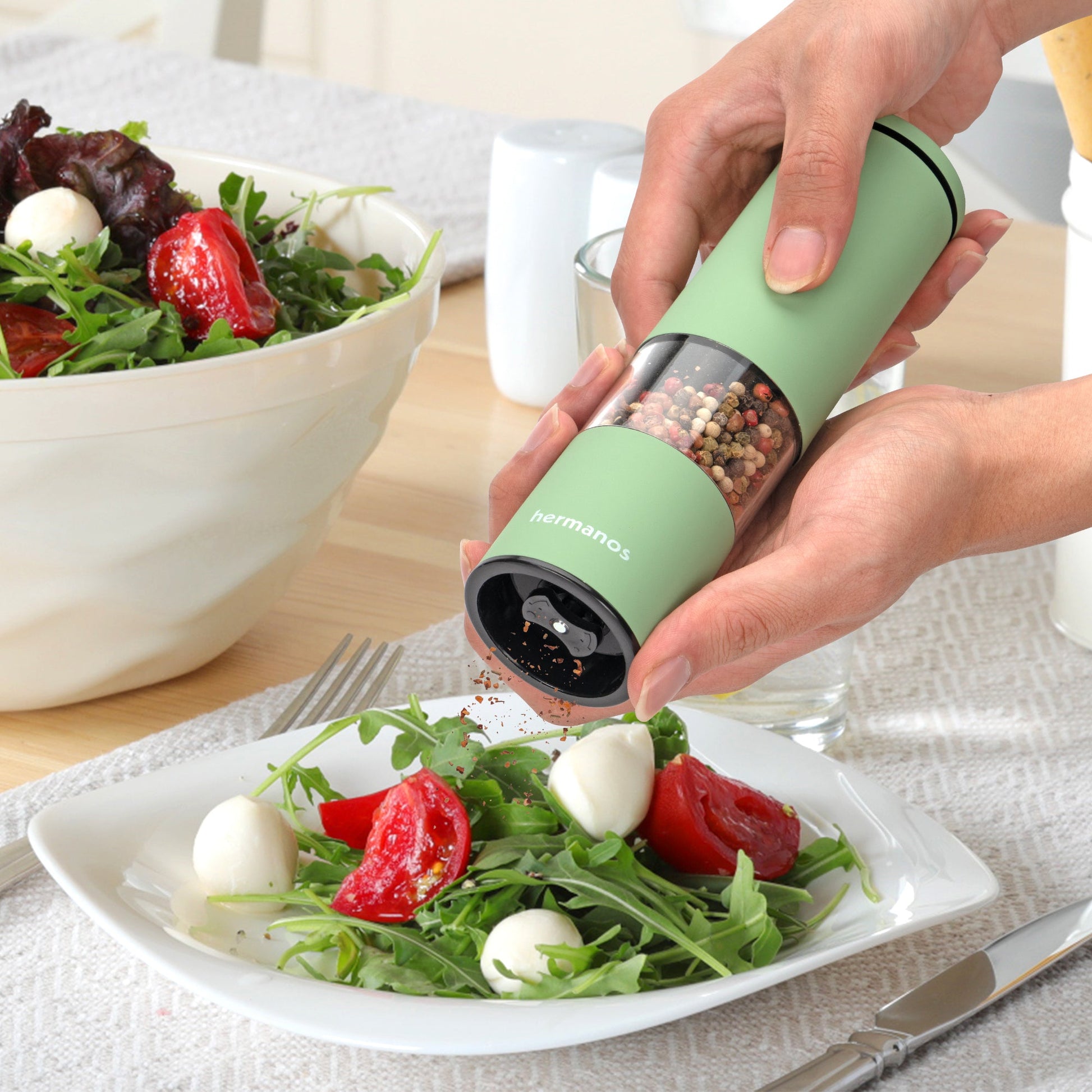 Groene hermanos elektrische pepermolen en zoutmolen met transparante cilinders, gevuld met gemengde peperkorrels en roze zoutkristallen, geschikt voor moderne keukens en gourmet kookplekken.