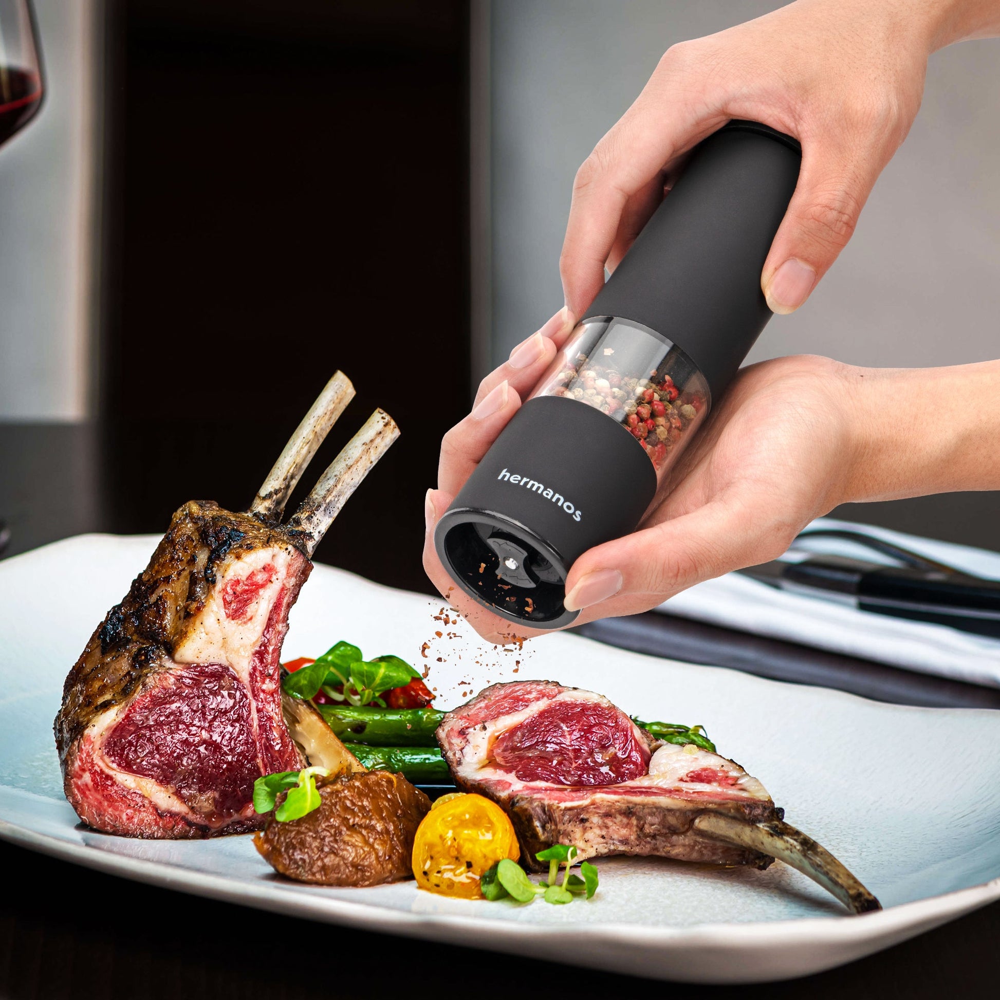 Zwarte Hermanos pepermolen en zoutmolen met transparante cilinders, gevuld met gemengde peperkorrels en roze zout. Ideaal voor moderne keukens en gourmet kookplekken.