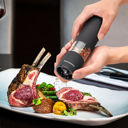 Zwarte Hermanos pepermolen en zoutmolen met transparante cilinders, gevuld met gemengde peperkorrels en roze zout. Ideaal voor moderne keukens en gourmet kookplekken.