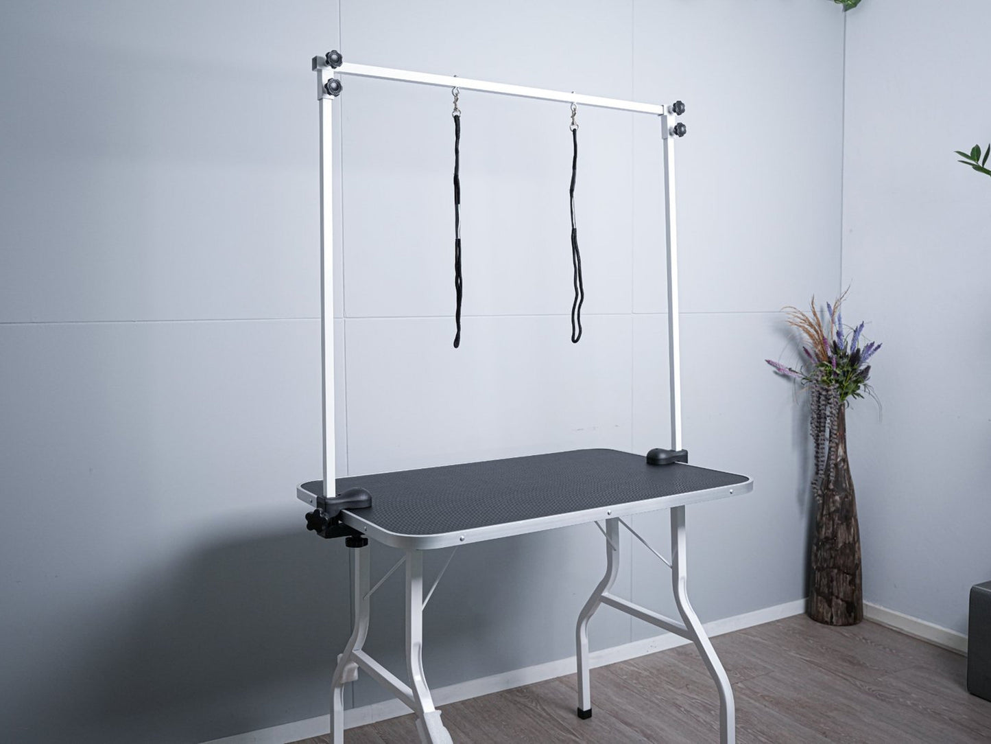 Een witte, vouwbare hondensnijtafel met zwarte oppervlak en hangende riemen, geschikt voor professionele hondendekking en thuisverzorging.
