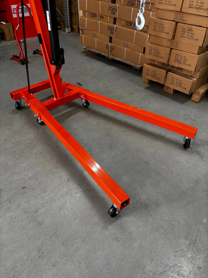 Een oranje, zwaarbelaste kraan met wielen, uitgerust met een ketting en haak, staat klaar voor gebruik in een magazijn. Geschikt voor professionele liftopdrachten en zware werkzaamheden in de logistiek.