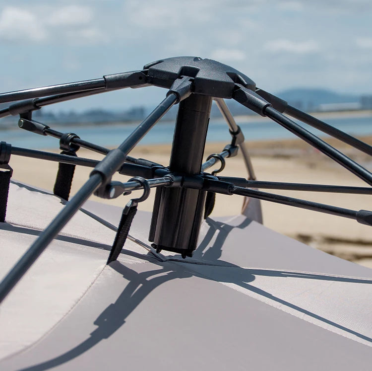 Zilveren vinyl zonnescherm met UPF60+ bescherming, opgesteld op het strand met twee vouwstoelen en tafel. Ideaal voor zonbescherming tijdens kamperen 