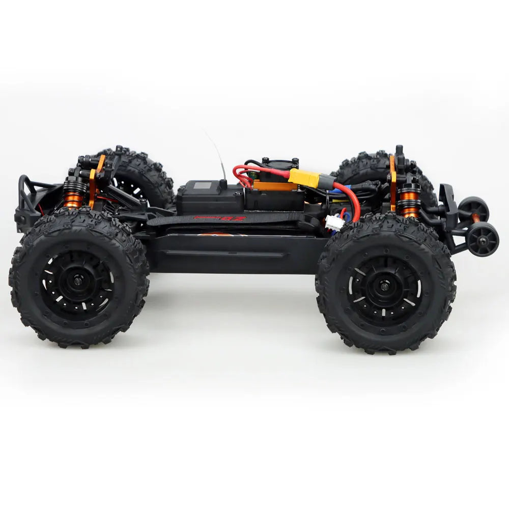 Oranje en blauwe RC monstertruck met grote zwarte banden en zichtbare “MT-16”-sticker, geplaatst naast zijn zwarte stuurunit voor terreinrijden. - Fot