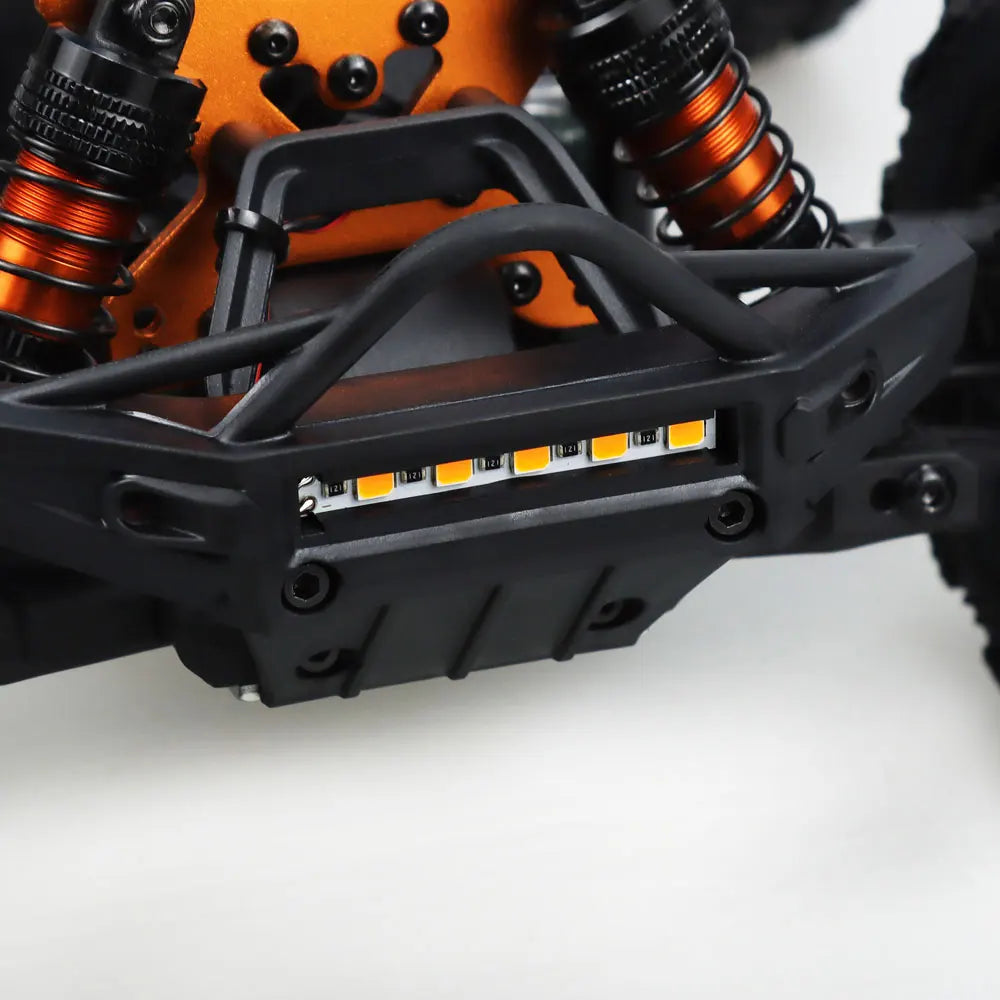 Oranje en blauwe RC monstertruck met grote zwarte banden en zichtbare 'MT-16' sticker, geplaatst naast zijn zwarte stuurunit voor speelplezier op zach