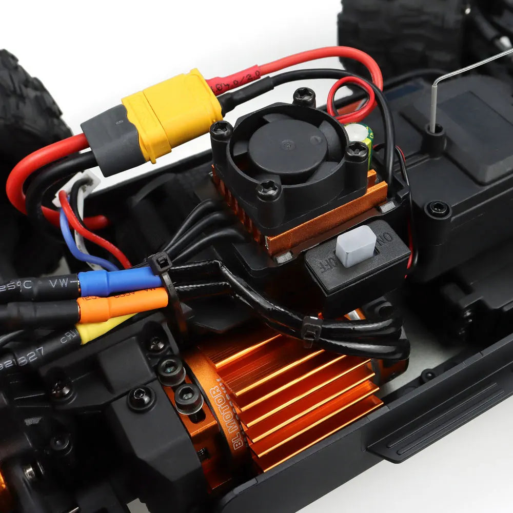 Oranje en blauwe RC monstertruck met grote zwarte banden en zichtbare "MT-16" sticker, naast een zwarte stuurunit voor speelplezier op zand of gras. -