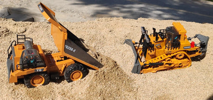 Grote, realistische RC-graafmachine in zwart en geel, met zichtbare trekkerbanden en schep die zand opvangt. Inclusief afbeeldingen van accessoires en