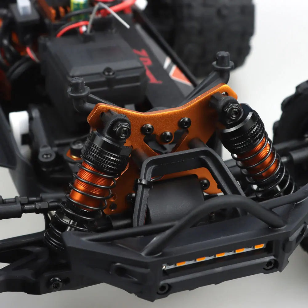Oranje en blauwe RC monstertruck met grote zwarte banden en zichtbare "MT-16" sticker, geplaatst naast zijn zwarte stuurunit voor speelplezier op zand
