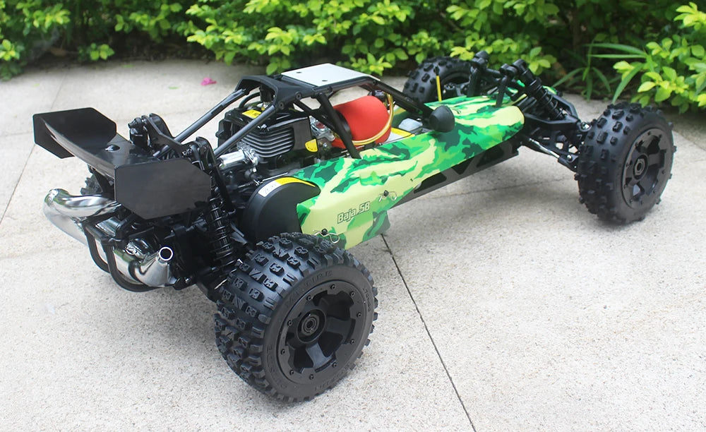 Groene camouflage RC buggy met zwarte banden en metalen frame, klaar voor terreinrijden. Zichtbare motor en stuurwiel voor speelplezier op zand of gra