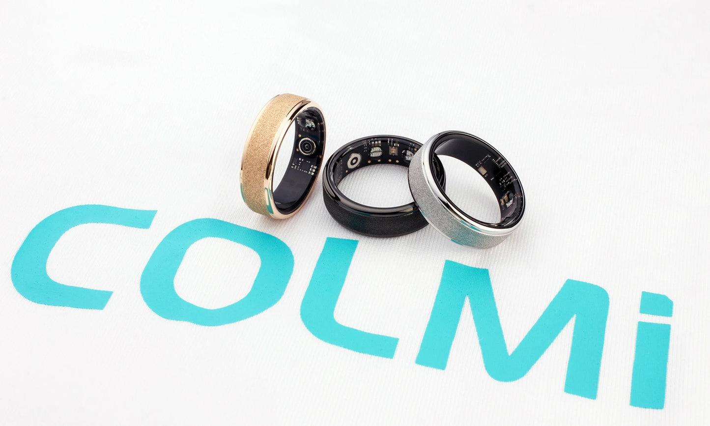 Een COLMi slimme ring in goudkleur met glinsterende textuur, naast een zwarte variant met zichtbare technische componenten, beide in een zwarte opbergdoos voor dagelijks gebruik en sportactiviteiten. - Foto 31