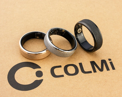 Een COLMi slimme ring in goudkleur met glinsterend oppervlak, naast een zwarte variant met zichtbare technische componenten, beide in een zwarte opbergdoos voor dagelijks gebruik en sportactiviteiten. - Foto 30