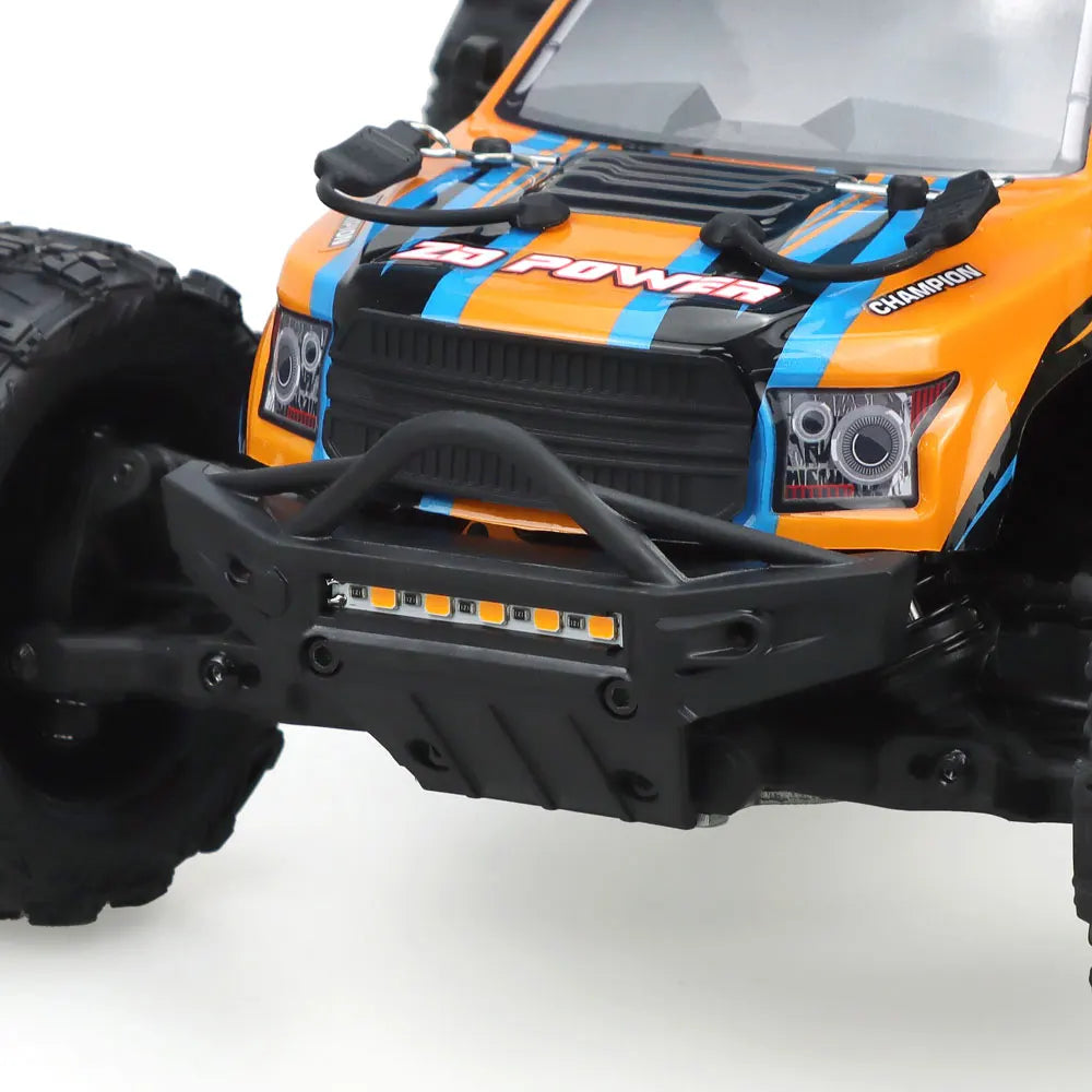 Oranje en blauwe RC monstertruck met grote zwarte banden en zichtbare "MT-16" sticker, geplaatst naast zijn zwarte stuurunit voor terreinrijden en spe