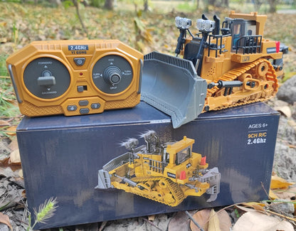 Grote, realistische RC-graafmachine in zwart en geel, met zichtbare trekkerbanden en een schep die zand opvangt. Inclusief afbeeldingen van de control