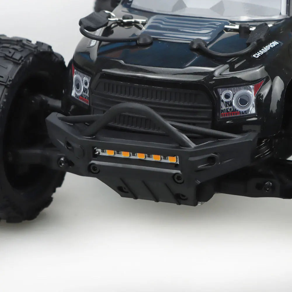 Oranje en blauwe RC monstertruck met grote zwarte banden en zichtbare "MT-16" sticker, geplaatst naast zijn zwarte stuurunit voor speelplezier op zand