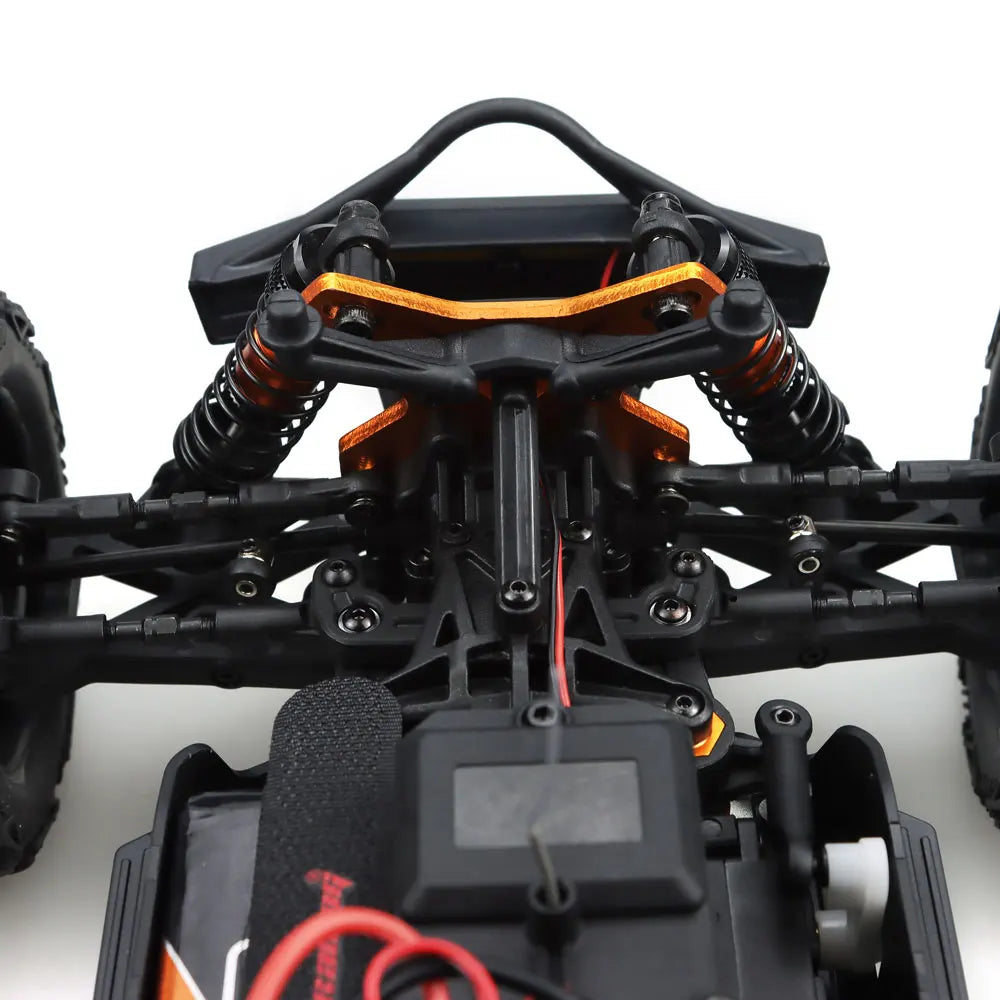 Oranje en blauwe RC monstertruck met grote zwarte banden en zichtbare "MT-16" sticker, geplaatst naast zijn zwarte stuurunit voor speelplezier op zand