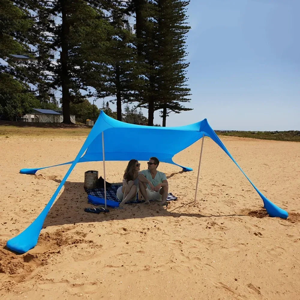 Blauwe zonnescherm tent met metalen stokken biedt schaduw op het strand. Vrouw in bikini en strohoed ontspant op een ligstoel onder de tent. - Foto 18