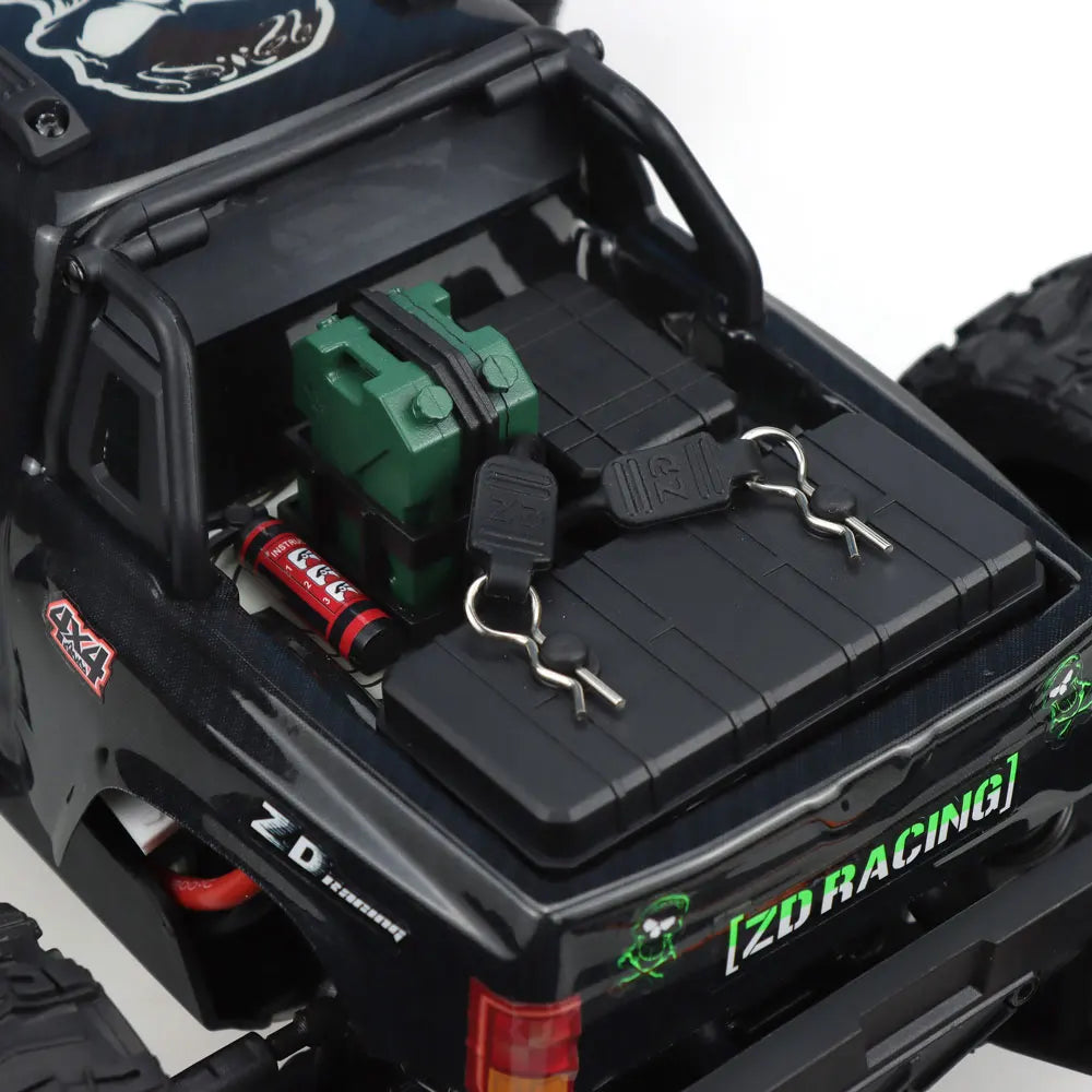Oranje en blauwe RC monstertruck met grote zwarte banden en zichtbare 'MT-16' sticker, geplaatst naast zijn zwarte stuurunit voor speelplezier op zand