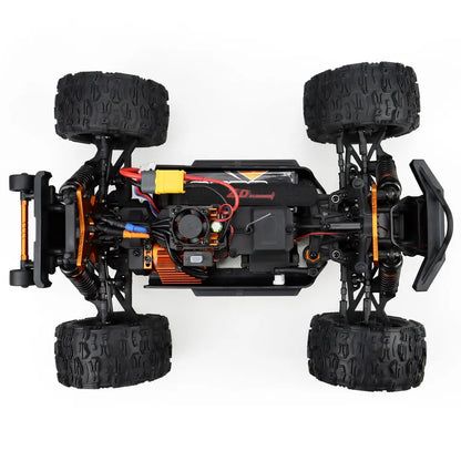 Oranje en blauwe RC monstertruck met grote zwarte banden en zichtbare "MT-16" sticker, geplaatst naast zijn zwarte stuurunit voor speelplezier op zach