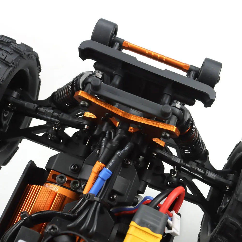 Oranje en blauwe RC monstertruck met grote zwarte banden en zichtbare 'MT-16' sticker, geplaatst naast zijn zwarte stuurunit voor speelplezier op zand