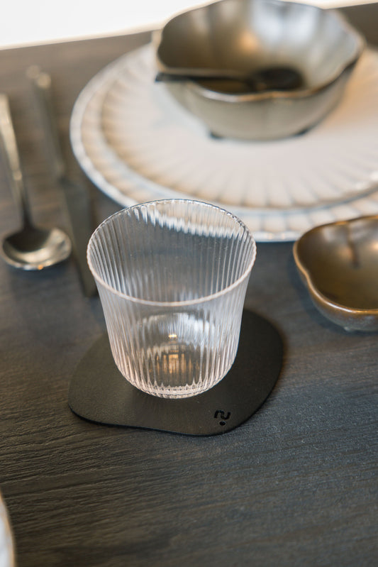 Donkerblauwe, ronde koffietafelmatjes van zacht leer liggen op een houten tafel. Ze zijn voorzien van een minimalistisch zwart logo en geschikt voor gebruik in een moderne woonkamer.