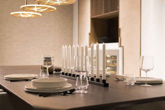 Een elegante tafelsetting met witte porseleinen borden, glazen en een zwart kandelaar met witte kaarsen, perfect voor een romantisch diner of feestelijke avondmaaltijd in een moderne eetkamer.