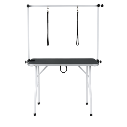 Een witte, vouwbare hondensnijtafel met zwarte oppervlakte en twee hangende riemen, geschikt voor professionele hondensnijden en -kapperij.