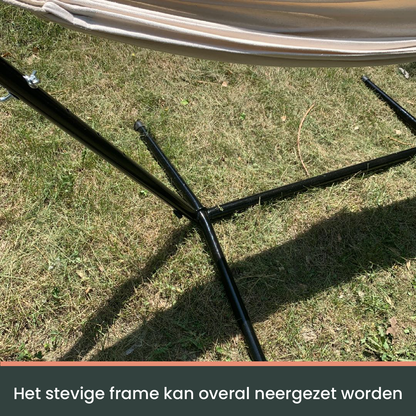 Een crèmekleurige hangmat met witte kabels hangt op een zwarte metalen standaard, ideaal voor ontspanning in de tuin of op het terras.