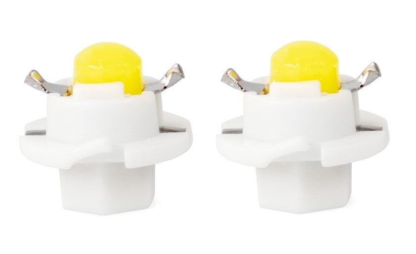 Geel LED-lampje met wit plastic behuizing en zilverkleurige contactpunten, geschikt voor auto’s en huishoudelijke verlichting. Twee identieke lampjes op witte achtergrond.