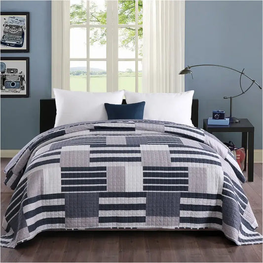 Een gestreept, patchwork dekbed in donkerblauw, grijs en wit, met zichtbare quilting en een moderne, geometrische stijl. Perfect voor een stijlvolle slaapkamer met een rustige, moderne sfeer.