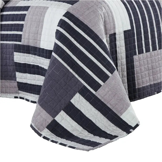 Een gestreept, patchwork dekbed in donkerblauw, grijs en wit, met zichtbare quilting en een moderne, geometrische print. Perfect voor een stijlvolle slaapkamer met een rustige, moderne sfeer.