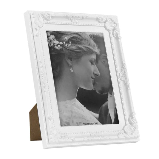 Een wit, klassiek fotolijstje met gedetailleerde reliëfversieringen, geschikt voor een bruiloftsfoto. Perfect voor het opbergen van herinneringen of als decoratief element in de woonkamer.