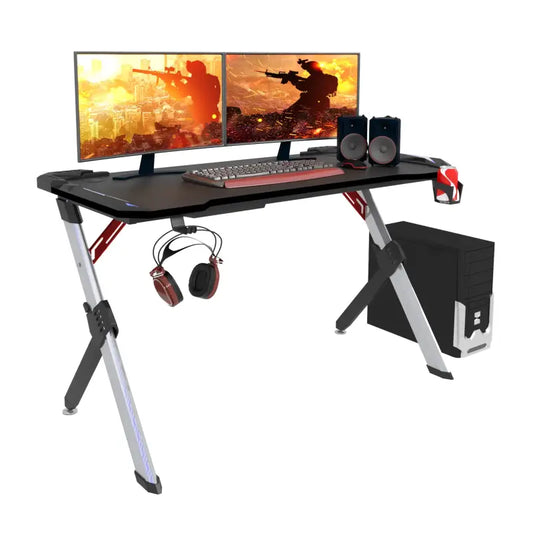 Gamingtafel met zwart glazen blad en zilveren X-vormige poten, uitgerust met twee schermen, koptelefoonhouder, speakers en een computer, speciaal ontworpen voor gaming en thuiswerk.