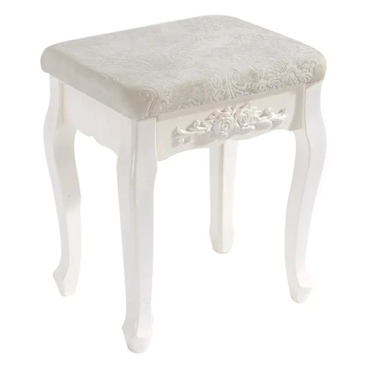 Een witte, klassieke houten kruk met gedetailleerde bloemenversiering en een zacht, crèmekleurig gestoffeerd zitvlak, perfect voor een elegante make-up of schoenenstijl in een slaapkamer.